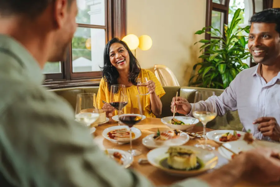 A woman laughs across a restaurant table set with small plates and wine.